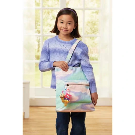 Girl wearing a purple jumper with a pastel coloured shoulder bag decorated with a hanging Aquabeads ice cream cone charm made from pink, yellow and purple beads.