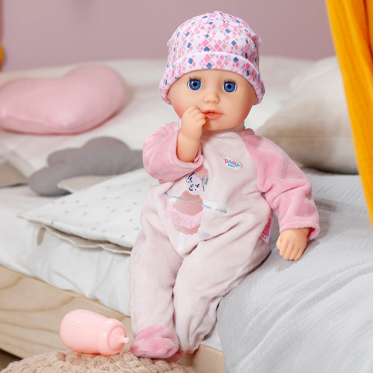 Baby Born Anna Rose doll seated on bed beside pink bottle