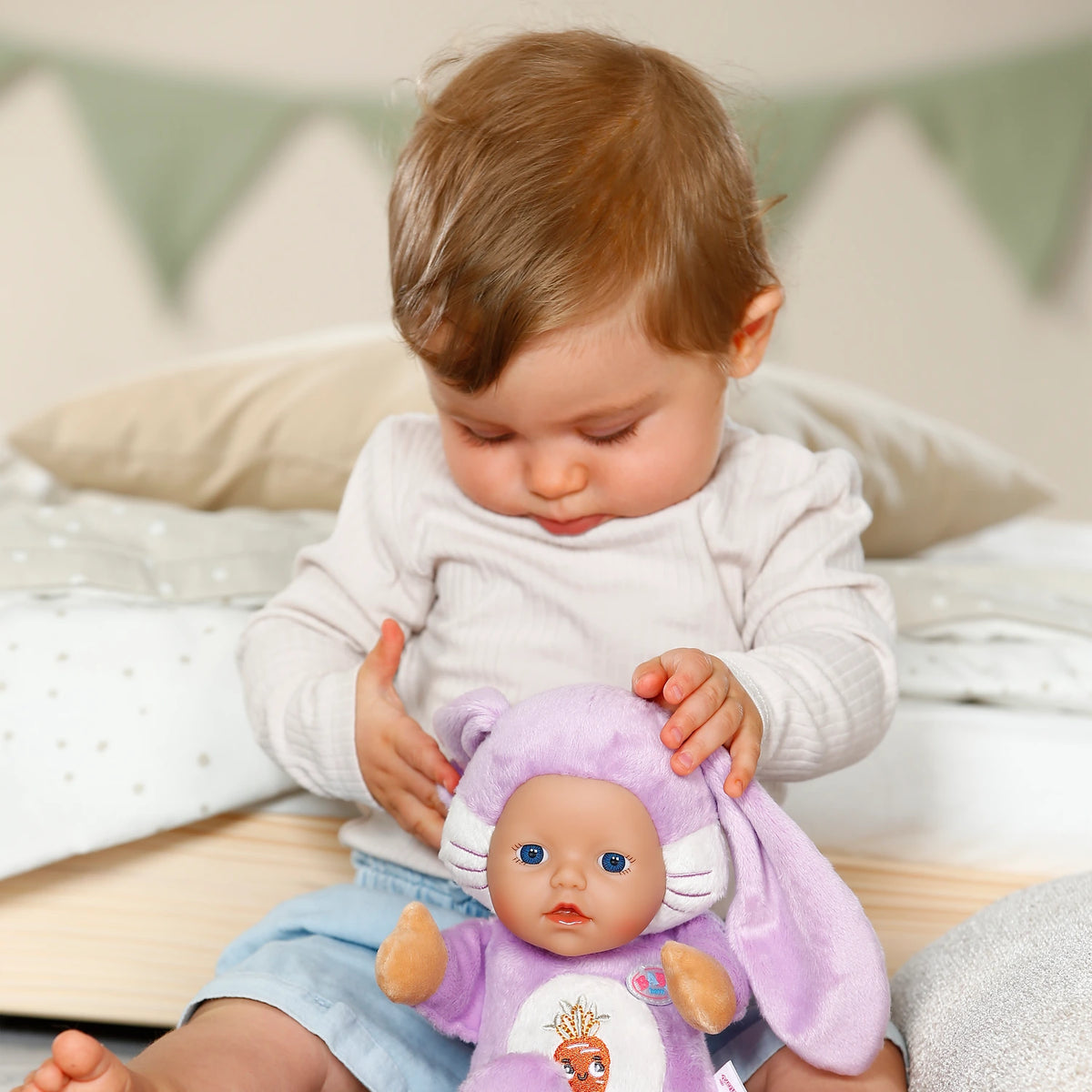 BABY born Funny Bunny doll held by child sitting on a bed