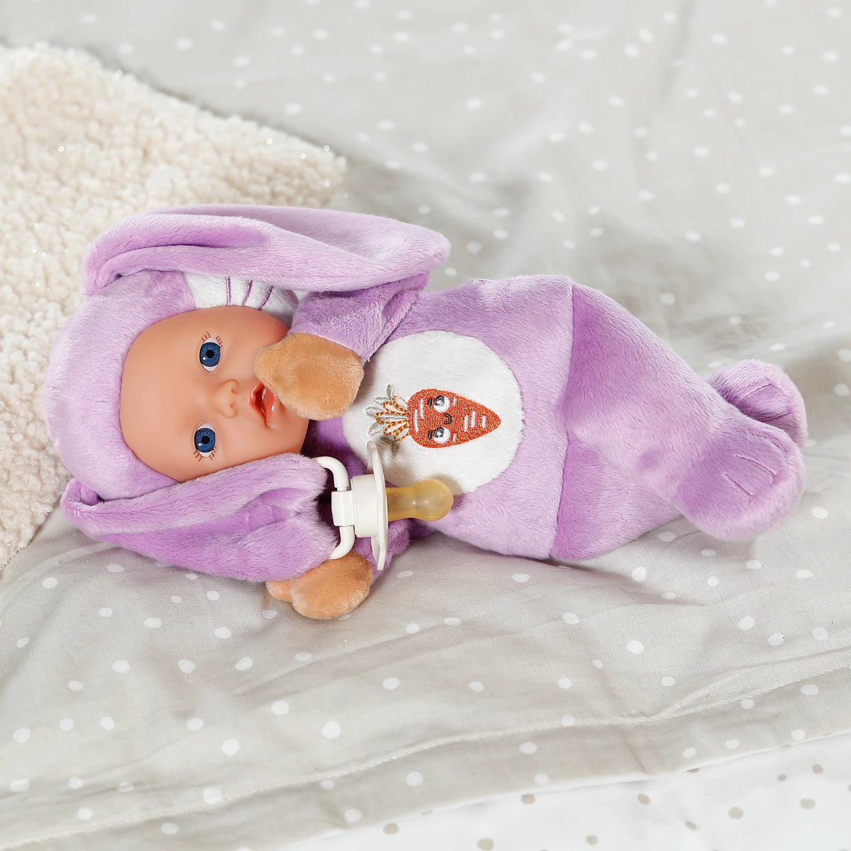 BABY born Funny Bunny lying on bed with dummy secured to the ear clip