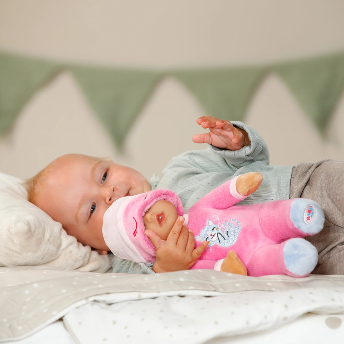 Baby Born For Babies Sleepy Pink doll held by baby lying on a bed