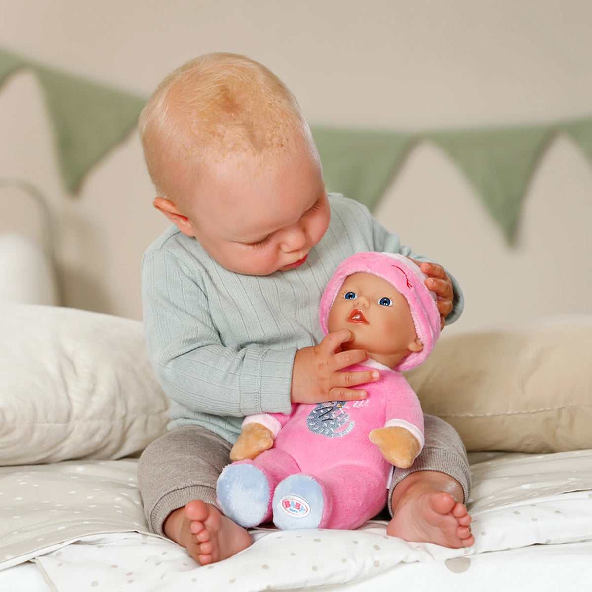 Baby Born For Babies Sleepy Pink doll on baby's lap with baby touching the doll's face