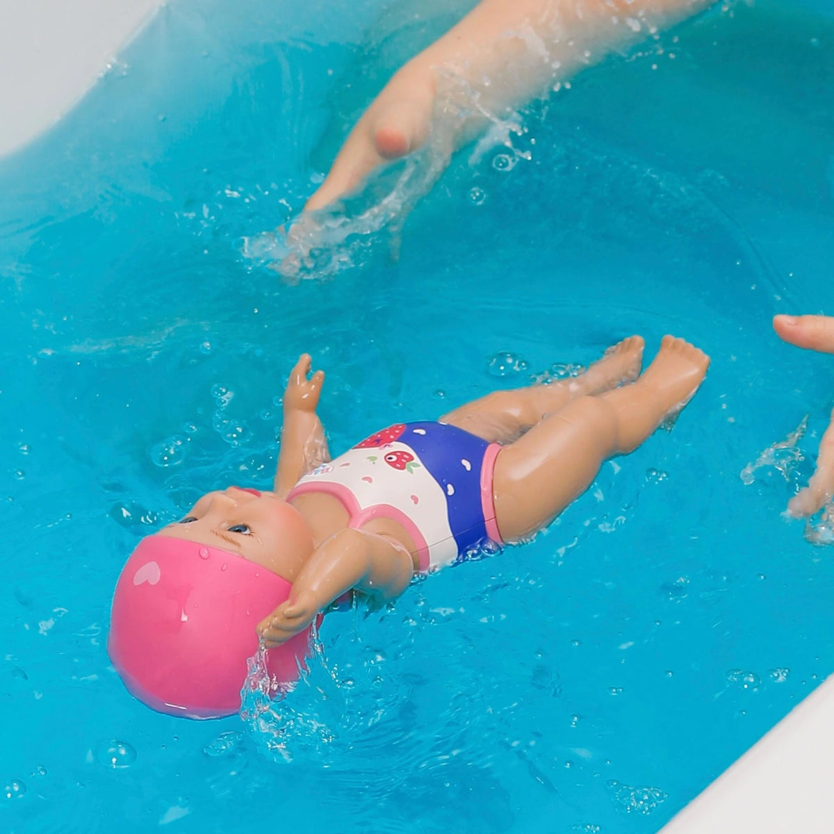 Baby Born Swimming Lizzie 30cm floating in blue pool water with hands guiding her