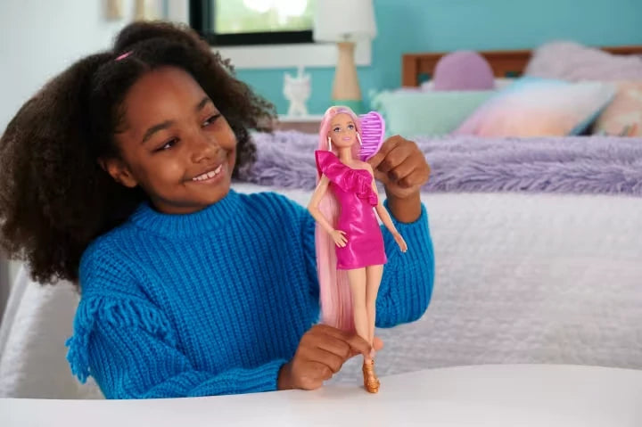 Child holding Barbie Fun & Fancy Hair Doll in a pink dress
