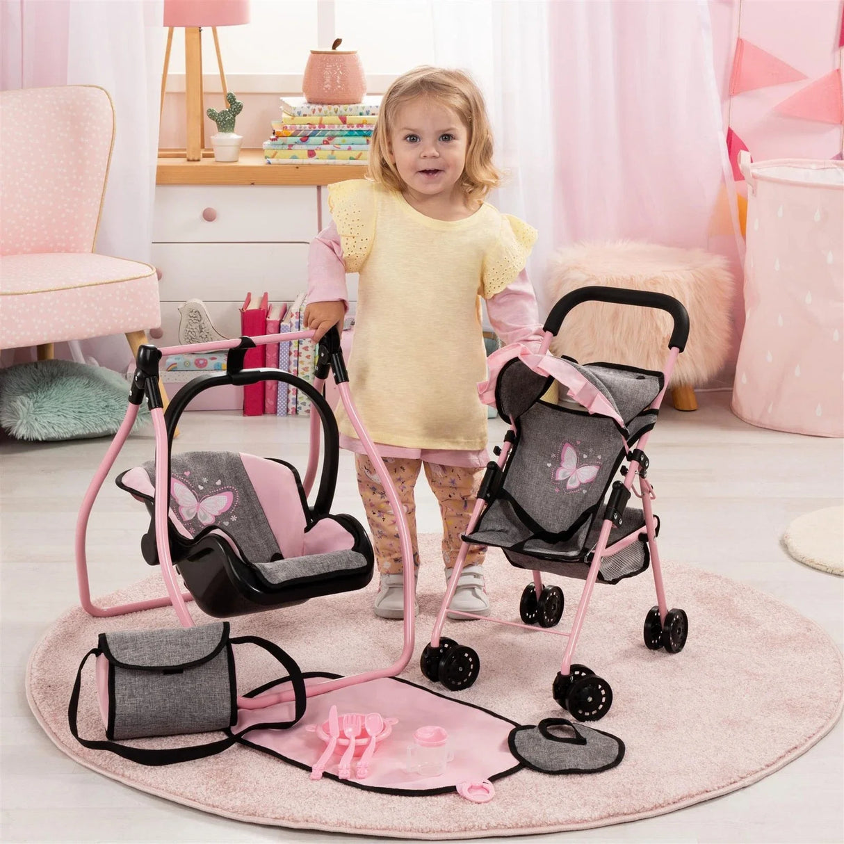 Young child playing with the grey and pink Bayer doll buggy and cradle set in a tidy playroom with soft pastel decor