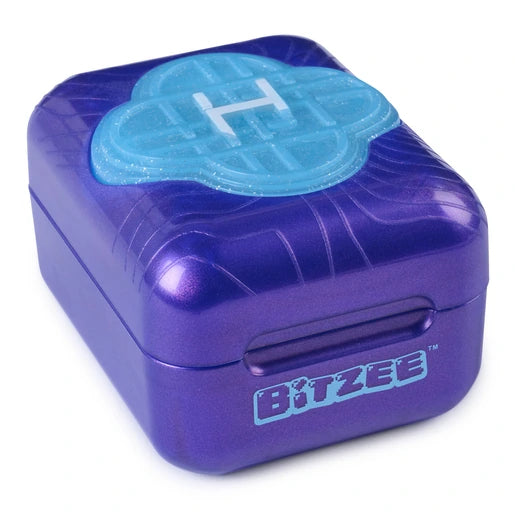 Angled view of the closed purple Bitzee KPop Demon Hunters pod, showing the turquoise Honmoon emblem, curved patterns on the lid and Bitzee logo on the front.