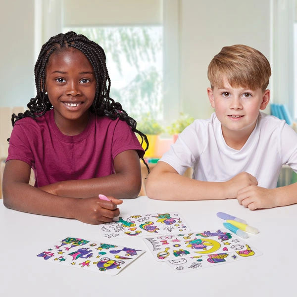 Two children using Brainstorm Colour Your Own Stickers Fairytale sheets and pens at a table