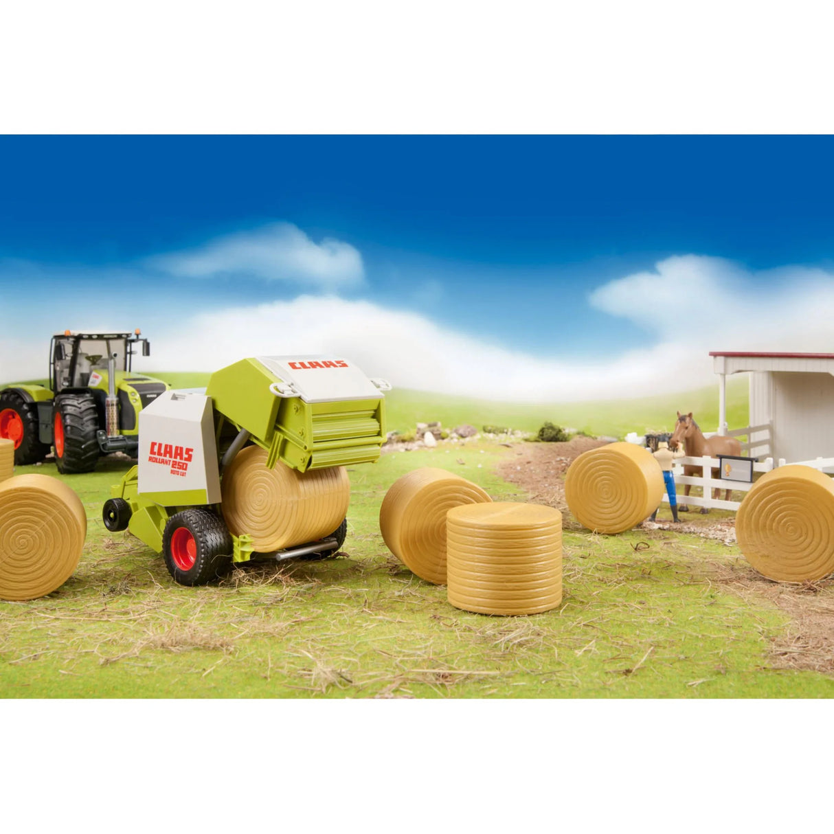 A toy Claas round baler on a grass field beside six ochre brown round hay bales and other farm toys.