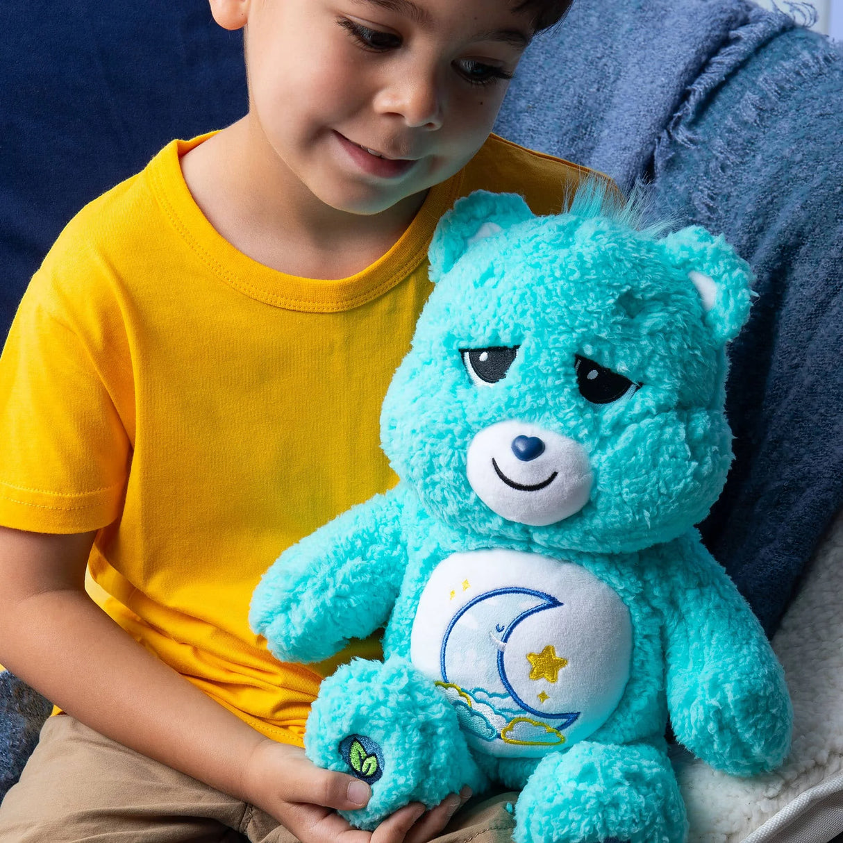 Child hugging Care Bears Cozy Bedtime Bear 14″ plush toy with sleepy moon and star belly badge in Ireland.