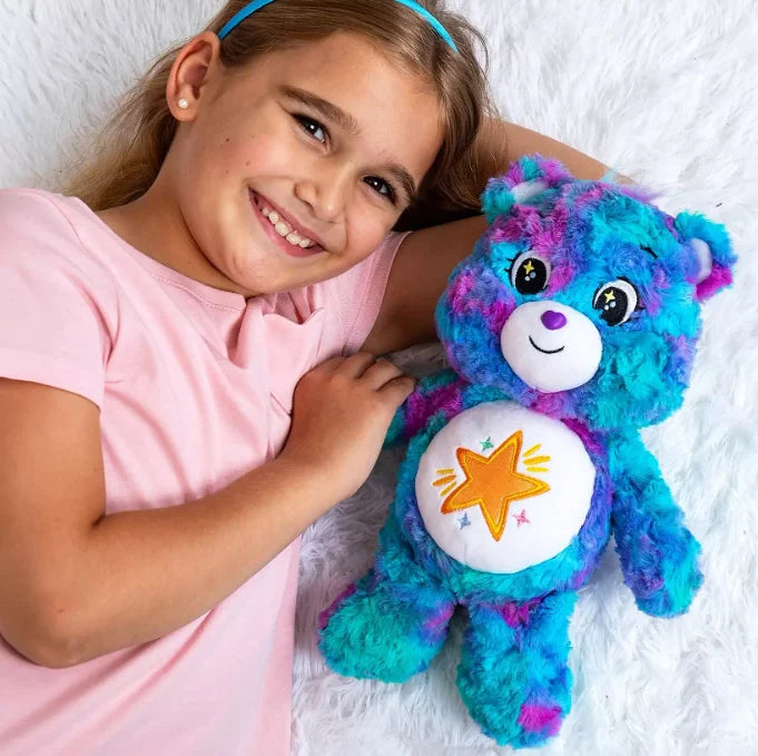 Child cuddling Care Bears Good Wishes Bear 35 cm plush toy with colourful tie-dye fur and gold star badge in Ireland.