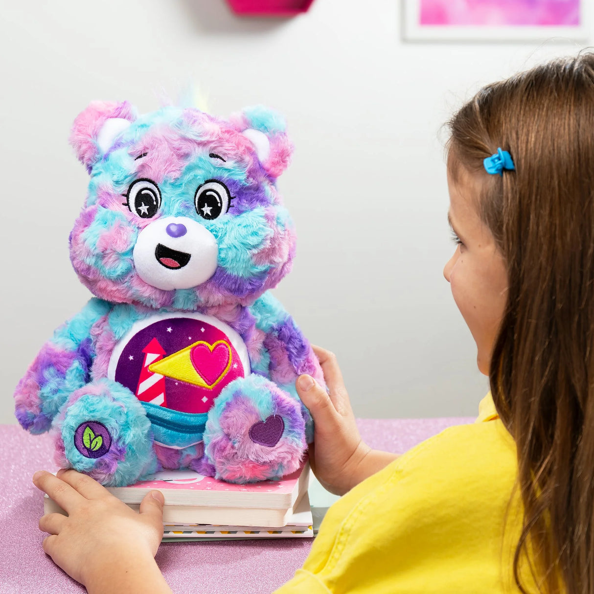 Girl playing with Care Bears Loveshine Bear plush toy at a table with pink sparkle surface in Ireland.