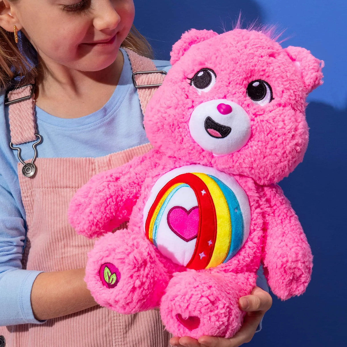 Child holding Care Bears Cozy Cheer Bear 14 inch plush to show large cuddly size and soft sherpa texture in Ireland.