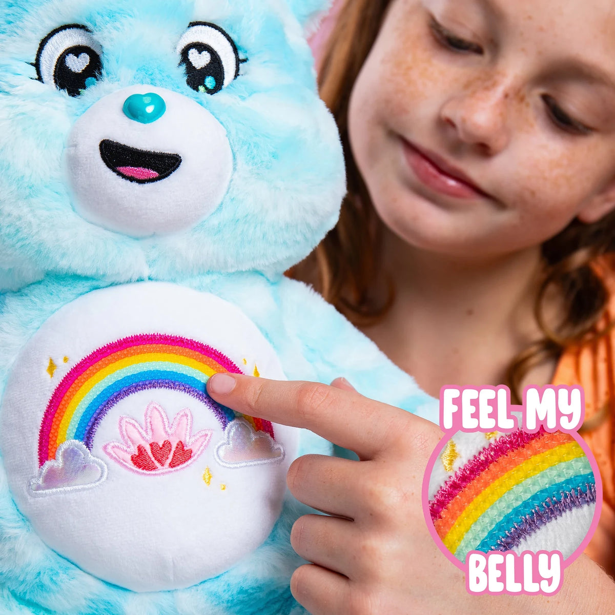 Child touching the colourful rainbow belly badge of Care Bears Sweet Serenity Bear, with an inset showing the raised sensory texture of the rainbow.