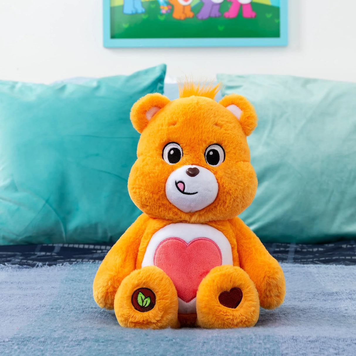 Care Bears Tenderheart Bear plush seated on bed with vibrant orange fur and red heart belly badge in Ireland.