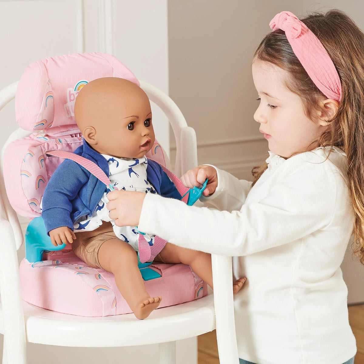 Casdon Baby Huggles Booster Seat with doll secured in the pink seat while a child fastens the teal buckle