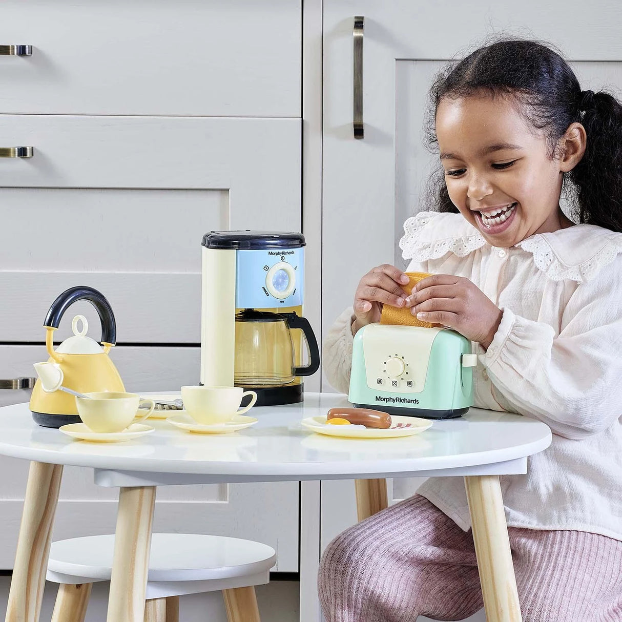Child playing with the Casdon Morphy Richards Kitchen Set toaster, kettle, coffee maker and play food on a table