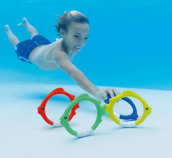 Child diving to collect colorful fish rings in swimming pool, Ireland