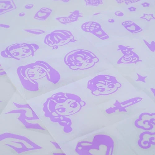 Close-up of purple KPop Demon Hunters temporary tattoo designs featuring cartoon character faces, microphones, hearts, stars, lightning bolts and other decorative symbols on translucent sheets.