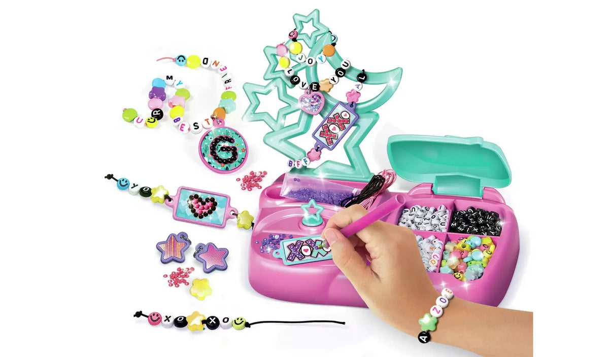 Crazy Chic Message Creations jewellery making activity showing a hand using a pink tool to decorate a charm on the pink workstation, surrounded by alphabet beads, star-shaped holder and completed bracelets.