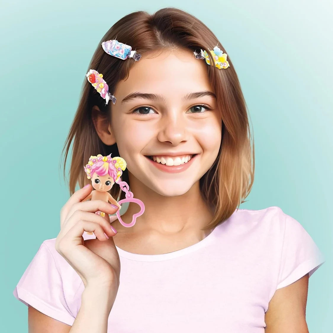 Smiling girl wearing three colourful Creamy Deco hair clips decorated with flowers, fruit slices and pearls, holding a pink haired baby doll attached to a heart shaped keychain.