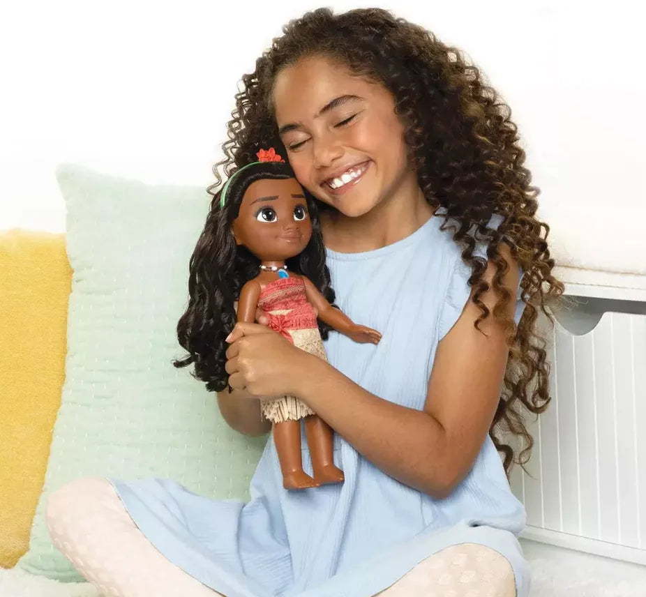 Child hugging Disney Princess Toddler Moana Doll dressed in red island dress with long hair and flower headband in Ireland.