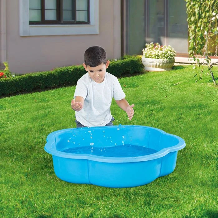 Child standing beside a blue shell shaped pool filled with water on grass