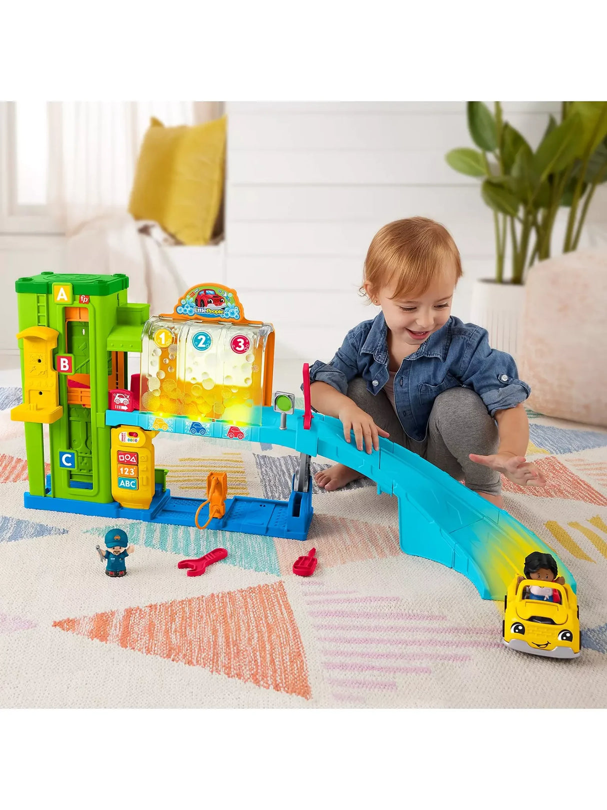 Toddler smiling while rolling a yellow Little People car down the ramp of the Fisher Price Light Up Learning Garage playset