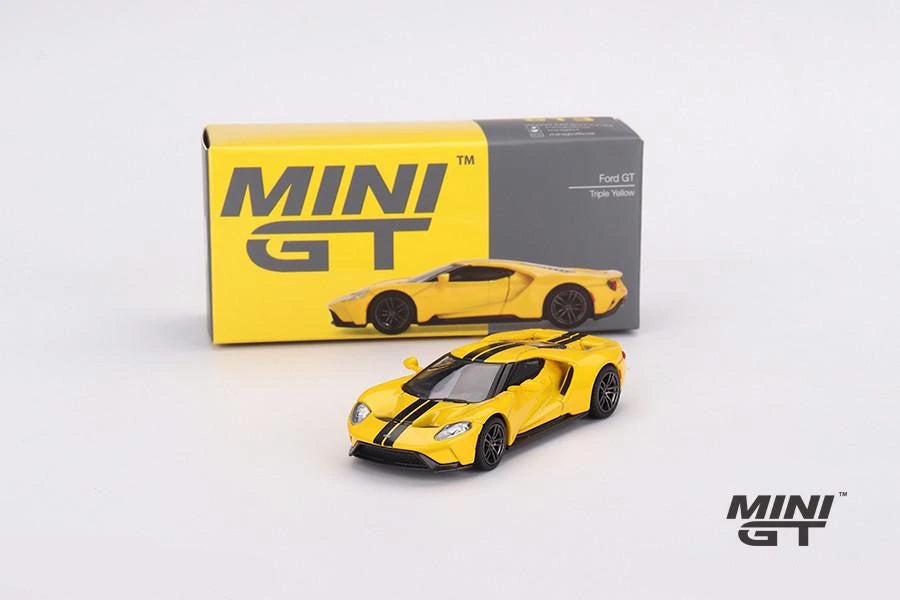 Ford GT Triple Yellow Mini GT model displayed in front of its box with the yellow body, black centre stripes and dark wheels visible