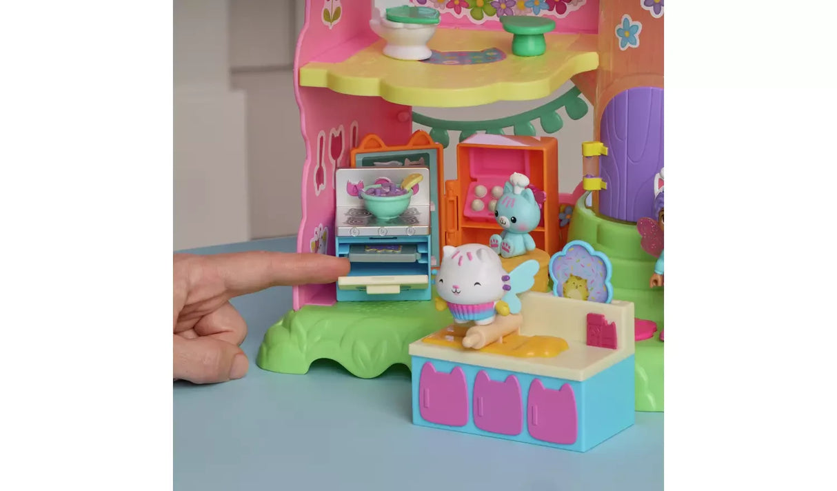 Hand sliding the grey baking tray into the open oven beside Cakey Cat on the rolling pin and the blue chef cat figure by the pink egg box