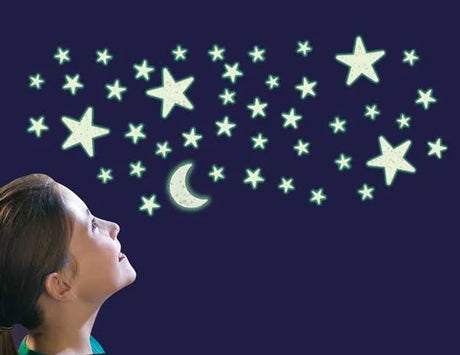 Bedroom scene with child looking up at glowing glitter stars and moon stickers shining on a dark wall.