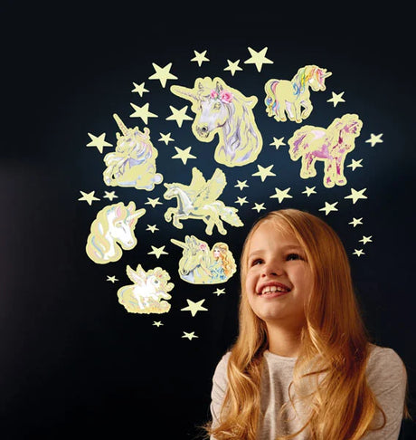 Smiling girl looking up at glowing unicorn and star stickers arranged on a dark wall in a circular pattern