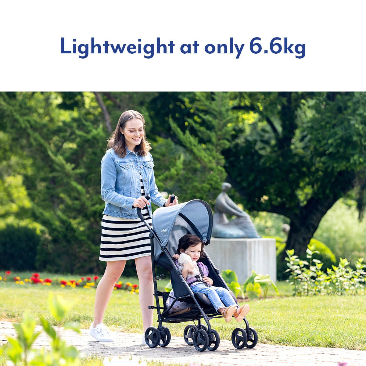 Woman pushing a child in a Graco EZLite Midnight stroller in a garden park