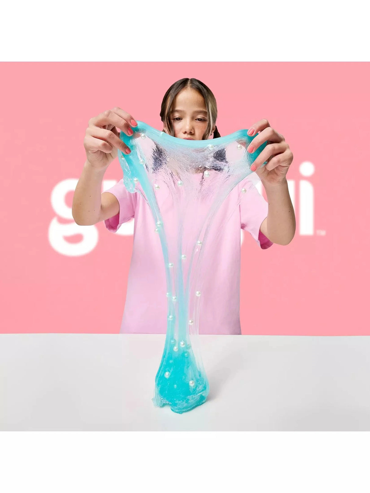 Gui Gui Deluxe Twin Pack teal clear shimmer slime stretched wide with white pearl beads embedded throughout, pulled upward from a white surface