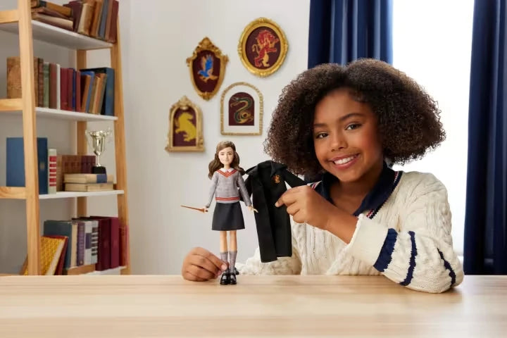 Child holding the removable Gryffindor robe beside the Hermione Granger fashion doll