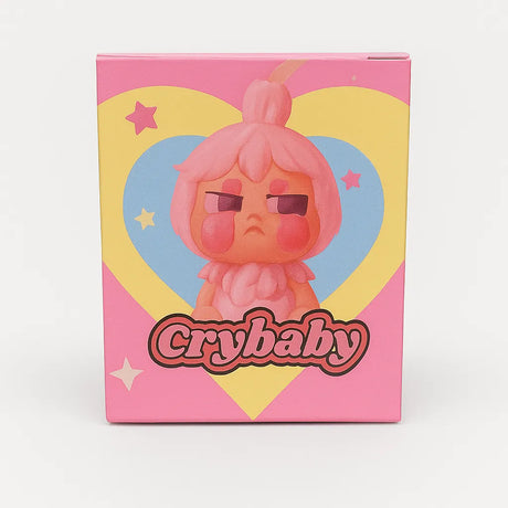 L Monsters collectible toy packaging featuring a grumpy pink cartoon character with rosy cheeks in front of a yellow and blue heart and stars, labeled ‘Crybaby’.