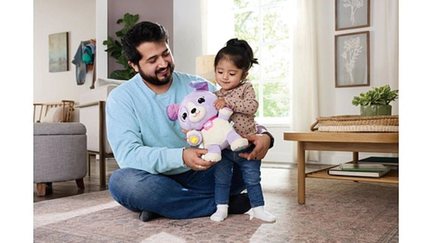 Man sitting on the floor with a toddler on his lap, holding the LeapFrog My Best Pal Violet purple interactive puppy