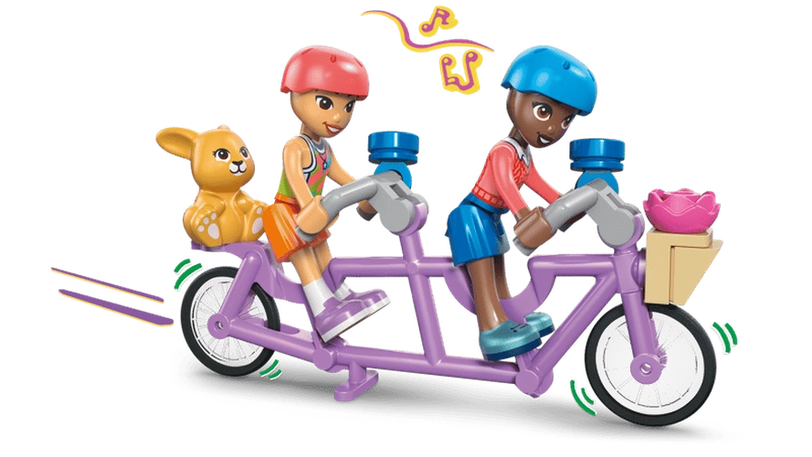 Two LEGO Friends minidolls wearing pink and blue helmets riding a purple tandem bicycle, with a brown bunny in the rear basket and pink flower in the front basket.