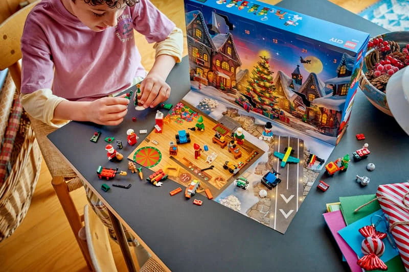 Child building LEGO City Advent Calendar mini models at a table with the opened calendar behind
