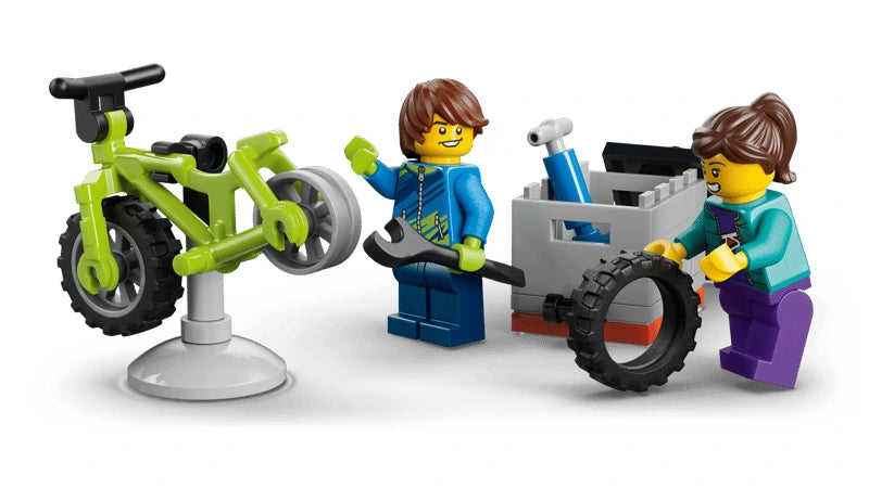 Two LEGO minifigures repairing a green mountain bike with a spare tyre and tool
