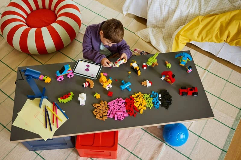 Child at a table with LEGO bricks, built models and drawing materials
