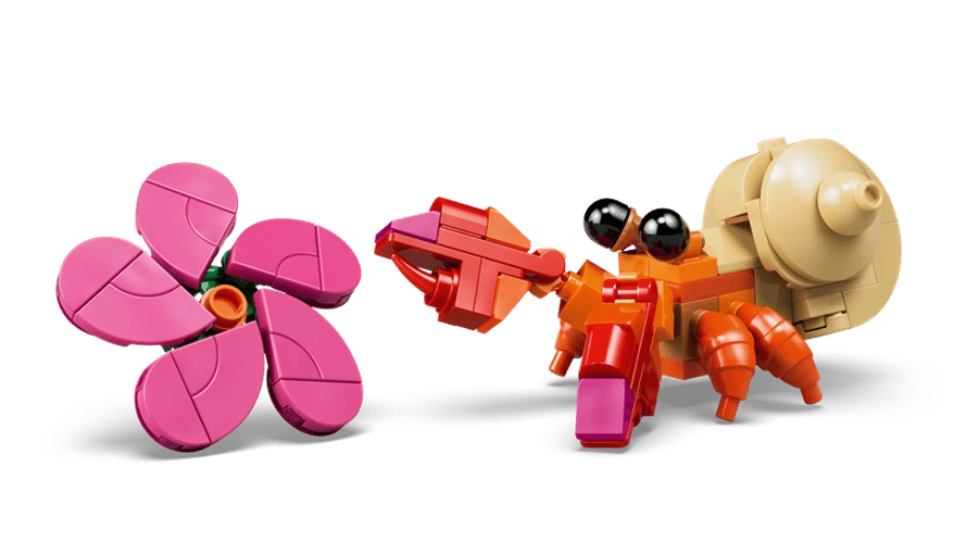 Close-up of the small orange LEGO Disney hermit crab with black eyes, beige shell and red claws beside a brick-built pink flower with five petals.
