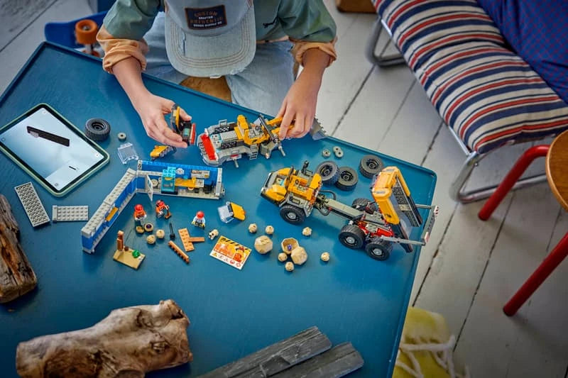 Child building a LEGO construction set at a table with dump truck, front end loader, minifigures and rock pieces