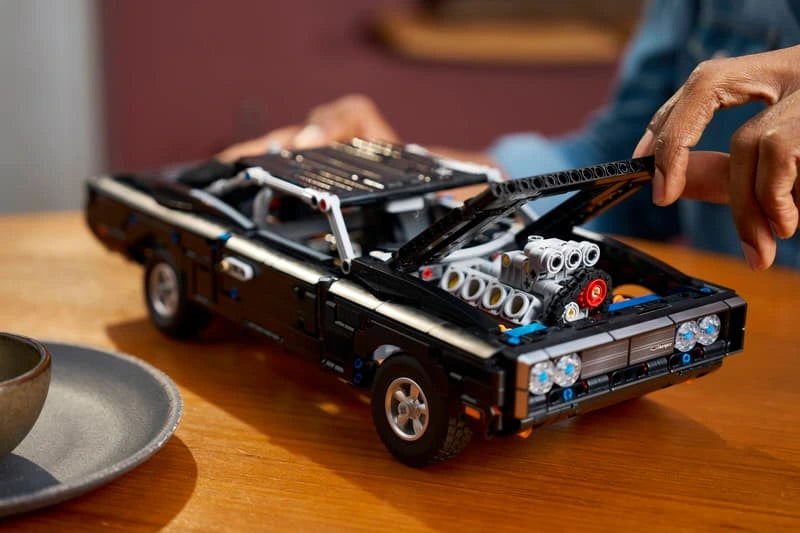 Person building LEGO Technic Dodge Charger R/T car at a table with model pieces visible