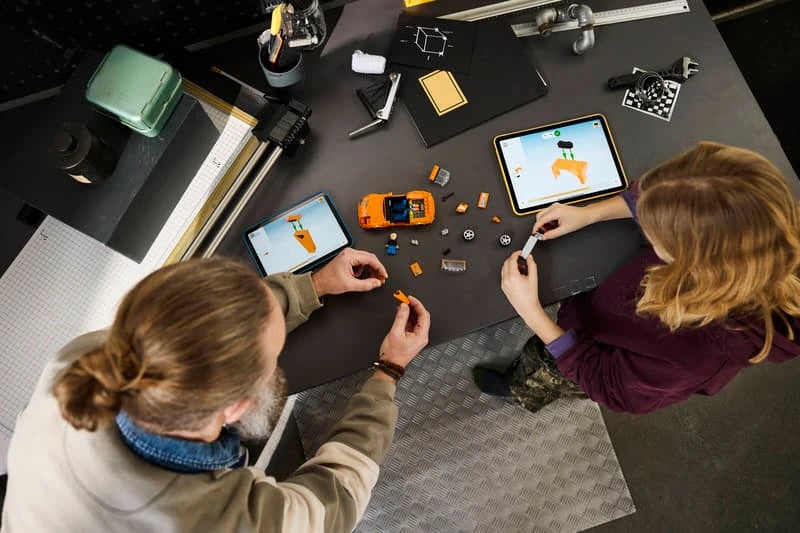 Child building a LEGO orange car set at a table with loose pieces and tablet instructions