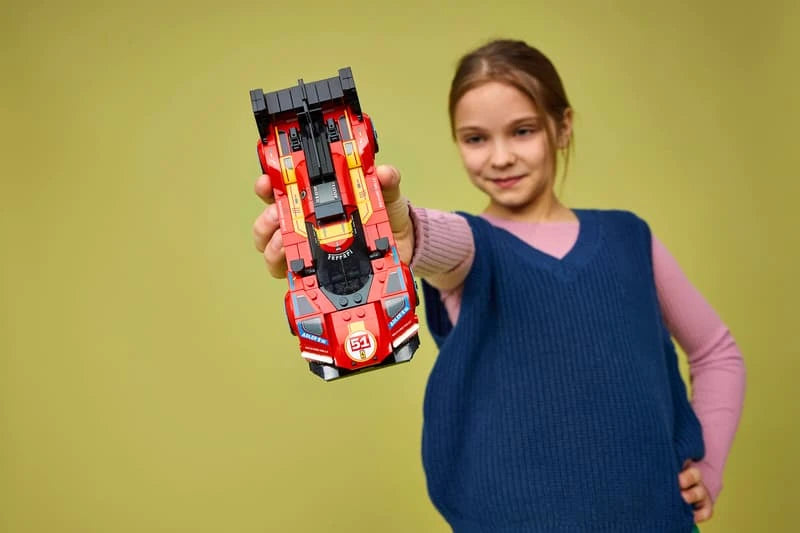 Child holding a LEGO Ferrari 499P race car model from the front