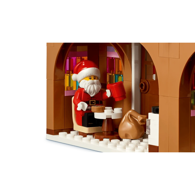 LEGO Santa minifigure seated inside the gingerbread house with a red mug, small table and brown sack