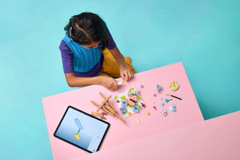 Child building LEGO Floral Art Decor Painting at a table with loose pieces and tablet visible