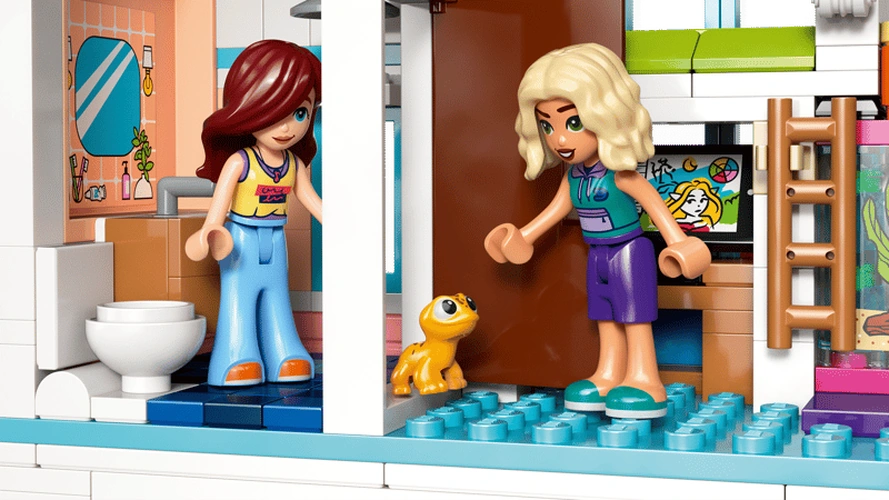 Close up of LEGO Friends Liann's Family House 42687 upstairs interior showing two minidolls, pet gecko, bedroom furniture, ladder and adjoining bathroom with toilet and washbasin.