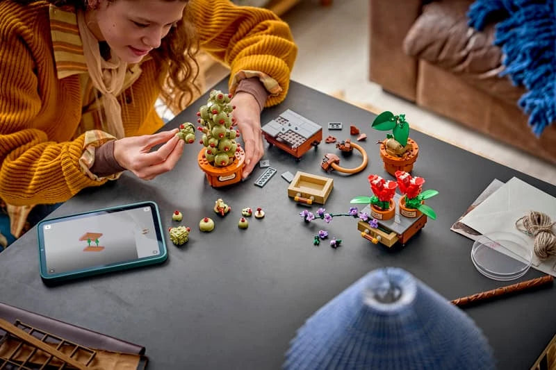 Children building a LEGO Harry Potter plant set at a table with pieces, tablet instructions and potted plant models