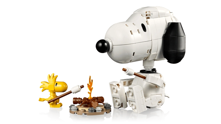 LEGO Snoopy seated opposite yellow Woodstock beside a small campfire, with both characters holding roasting sticks.
